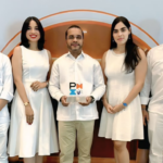 Cinco personas posan ante la gráfica de un evento; una sostiene un trofeo con la marca PMI.