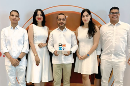 Cinco personas posan ante la gráfica de un evento; una sostiene un trofeo con la marca PMI.