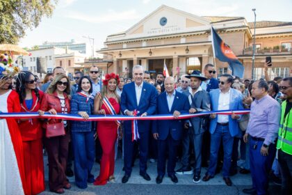 Participantes junto a una cinta roja, blanca y azul, con banderas y un edificio al fondo.