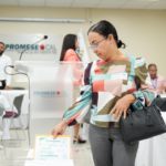 Persona introduce un sobre de oferta en una urna transparente en un salón de Promese/Cal.