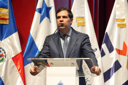 Ponente ante un atril y varias banderas durante una actividad institucional.