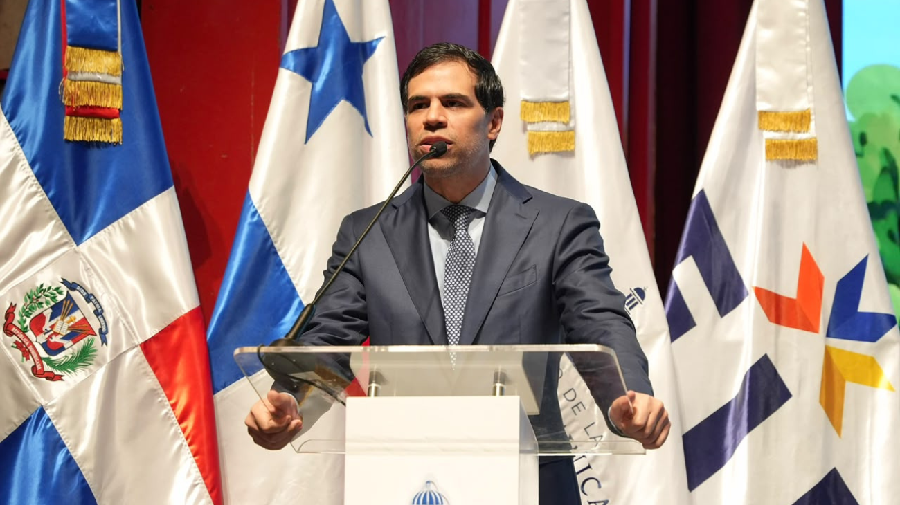 Ponente ante un atril y varias banderas durante una actividad institucional.