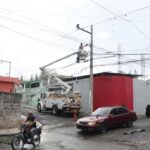 Cuadrilla con camión canasta interviene un poste junto a una vía urbana.