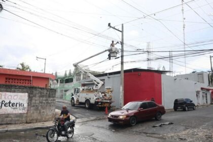 Cuadrilla con camión canasta interviene un poste junto a una vía urbana.