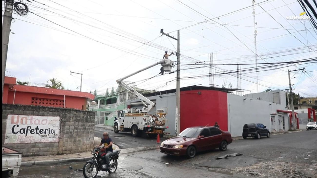 Cuadrilla con camión canasta interviene un poste junto a una vía urbana.