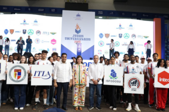Grupo con carteles de universidades ante un escenario deportivo.