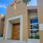 Fachada de una capilla con cruz, rótulo Divina Misericordia y placa institucional.