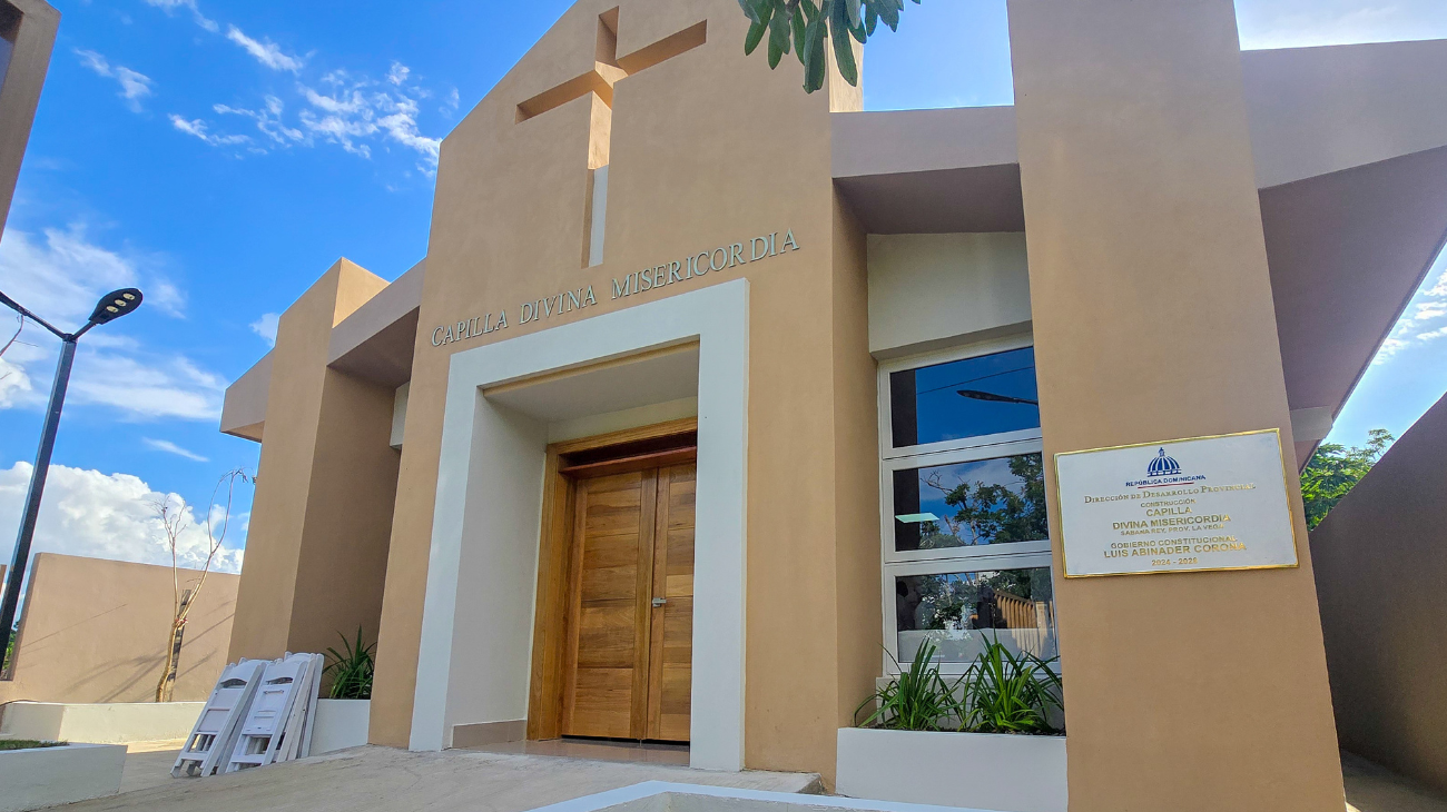 Fachada de una capilla con cruz, rótulo Divina Misericordia y placa institucional.