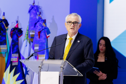Orador en un atril con banderas y señalética institucional.