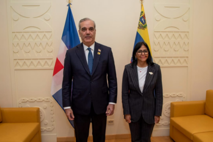 Dos personas posan entre las banderas de República Dominicana y Venezuela, en una sala con sofás.