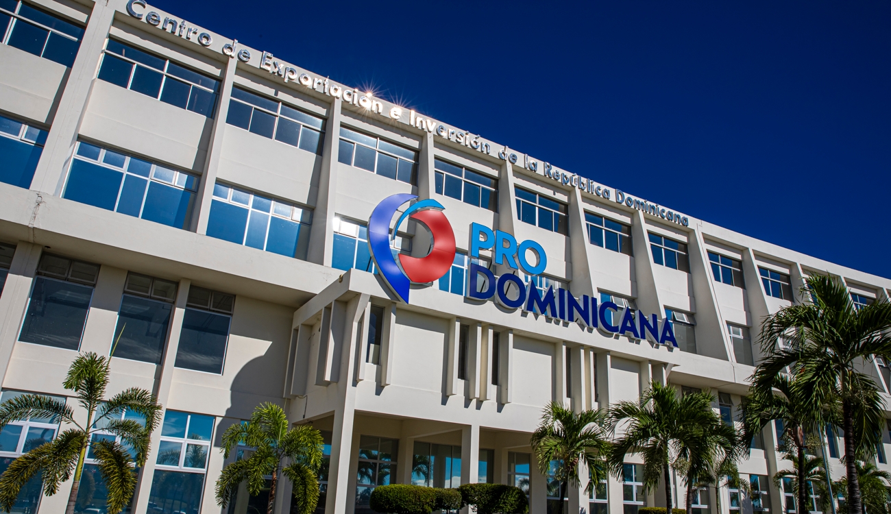 Fachada de un edificio con el logotipo ProDominicana, ventanas y palmeras en primer plano.