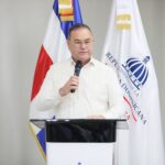 Persona con micrófono detrás de un atril, ante las banderas dominicana e institucional.