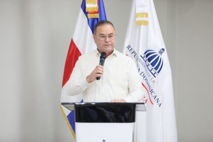 Persona con micrófono detrás de un atril, ante las banderas dominicana e institucional.