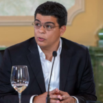 Persona en una mesa institucional con micrófono.