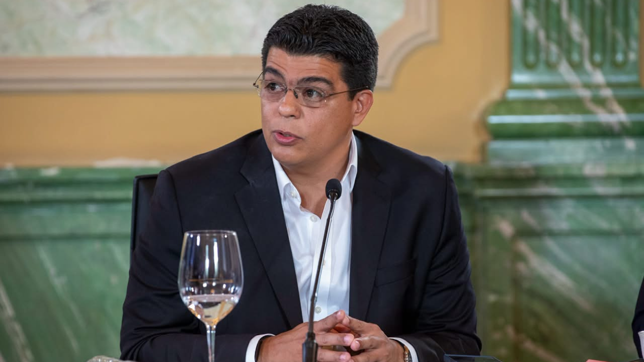 Persona en una mesa institucional con micrófono.