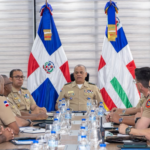 Militares uniformados se reúnen a ambos lados de una mesa, con dos banderas al fondo.