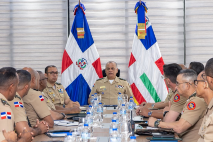 Militares uniformados se reúnen a ambos lados de una mesa, con dos banderas al fondo.