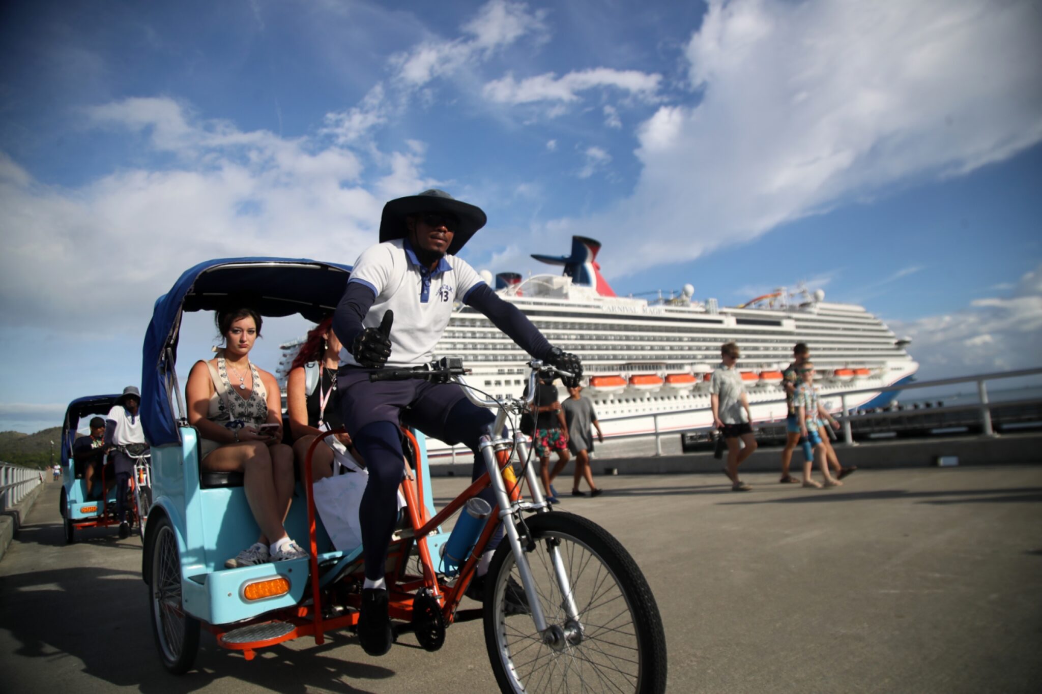 Bicitaxi, peatones y un crucero junto al muelle.