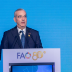 Orador ante dos micrófonos y un atril con el emblema de la FAO, sobre un fondo azul.