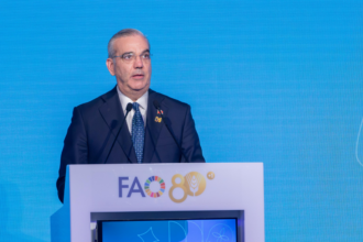 Orador ante dos micrófonos y un atril con el emblema de la FAO, sobre un fondo azul.
