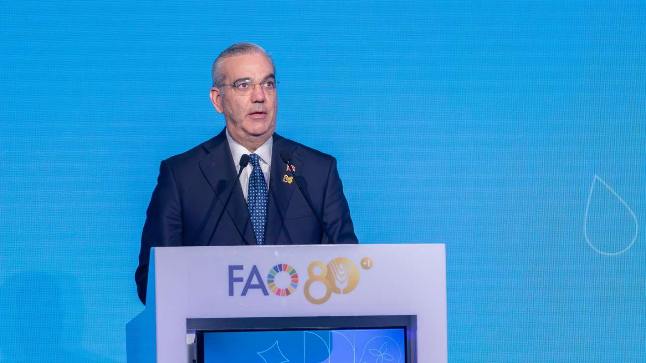 Orador ante dos micrófonos y un atril con el emblema de la FAO, sobre un fondo azul.