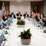 Participantes levantan las manos durante una reunión alrededor de una mesa.