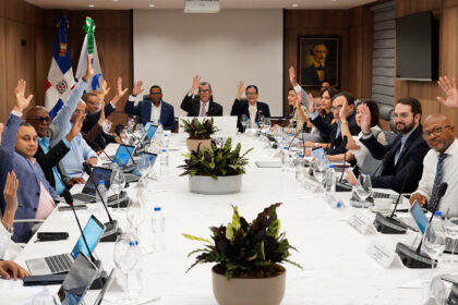 Participantes levantan las manos durante una reunión alrededor de una mesa.