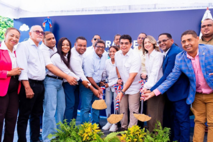 Participantes con palas y tierra ante un fondo institucional y plantas decorativas.