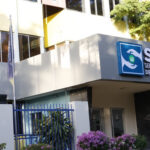 Fachada con letrero del Servicio Nacional de Salud, verja y banderas.
