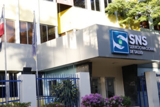 Fachada con letrero del Servicio Nacional de Salud, verja y banderas.