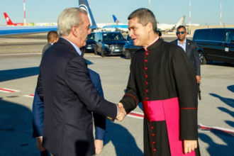 Saludo entre una persona con traje y otra con vestimenta clerical en un exterior aeroportuario.
