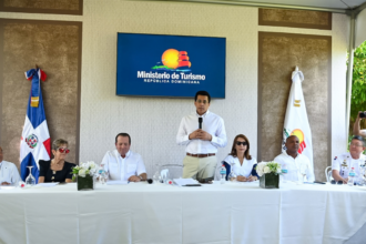 Participantes en una mesa y un ponente de pie, con pantalla del Ministerio de Turismo al fondo.