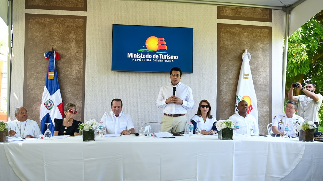 Participantes en una mesa y un ponente de pie, con pantalla del Ministerio de Turismo al fondo.