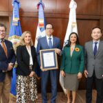 Cinco personas posan con un reconocimiento institucional enmarcado de la OEA.