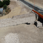 Vista aérea de un puente vial junto a muros de gaviones y un cauce.
