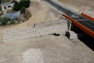 Vista aérea de un puente vial junto a muros de gaviones y un cauce.