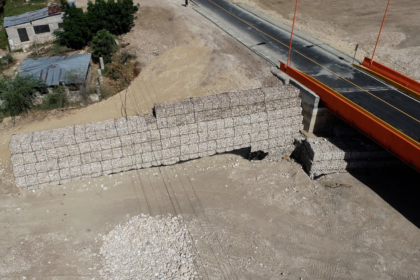 Vista aérea de un puente vial junto a muros de gaviones y un cauce.