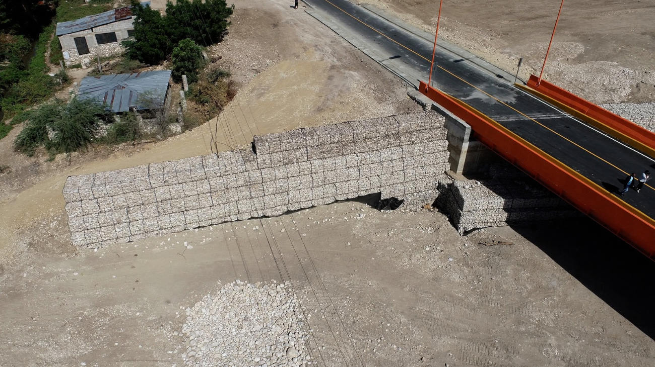 Vista aérea de un puente vial junto a muros de gaviones y un cauce.