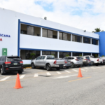 Fachada con letreros de Salud Pública, estacionamiento y vehículos.