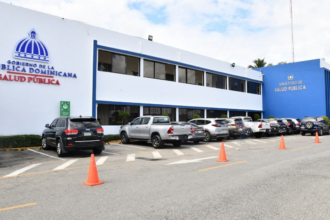 Fachada con letreros de Salud Pública, estacionamiento y vehículos.