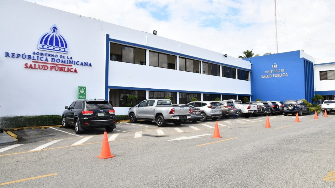 Fachada con letreros de Salud Pública, estacionamiento y vehículos.