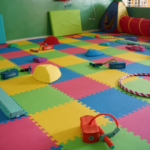 Aula vacía con suelo de espuma de colores, aros, túnel de juego y material de equilibrio.