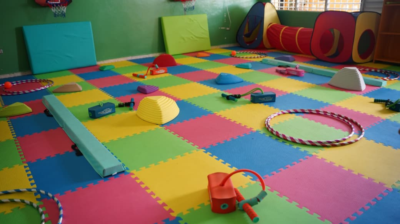 Aula vacía con suelo de espuma de colores, aros, túnel de juego y material de equilibrio.